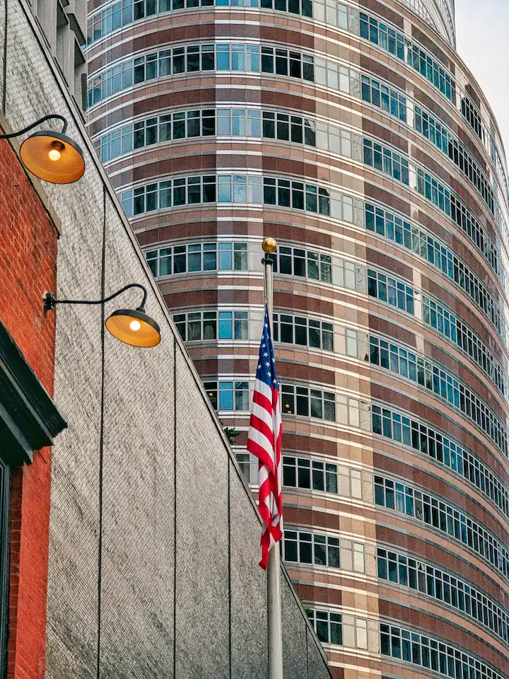 An American flag hans on a pole in front of a curved, red granite and glass facade of the Lipstick Building in NYC