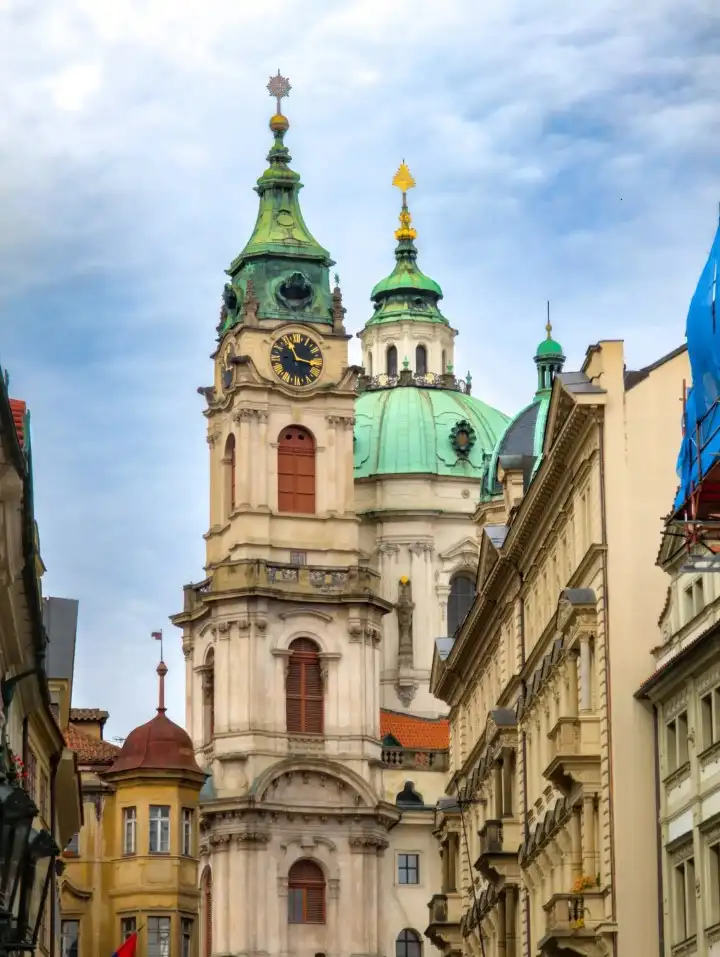A church with a clock tower and green copper domes, viewed from a city street